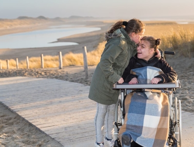 Disabled girl using wheelchair at the beach with her sister