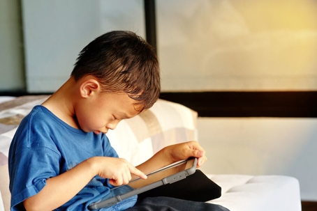 boy holding a tablet in a room alone
