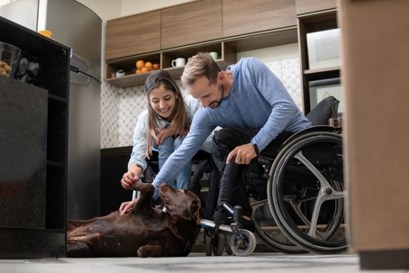 Couple who both use wheelchairs play with chocolate lab in their kitchen