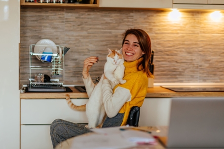 Young woman who uses wheelchair sits in her kitchen holding her cat