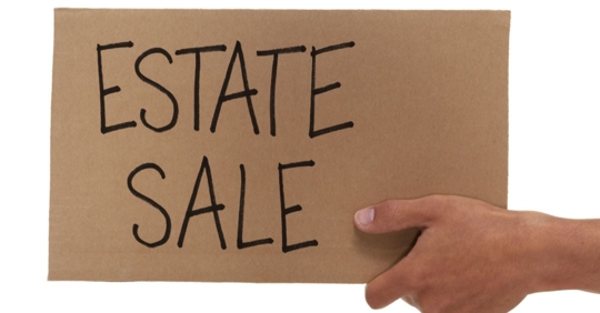 hand holding cardboard sign that has ESTATE SALE written on it
