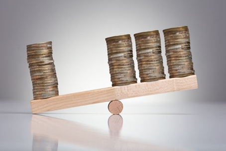 Stack Of Coins On Wooden Seesaw Over Gray Background