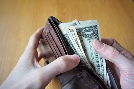 Male hand holding a leather wallet and withdrawing American currency (USD, US Dollars)