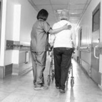 nurse and older woman walking down the hospital aisle